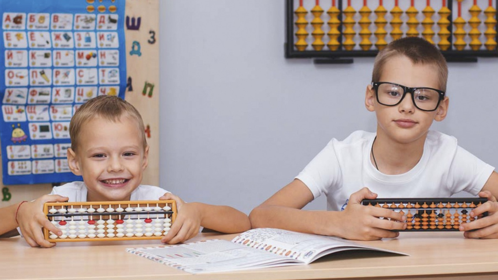 Dwóch chłopców znajduje się na sali lekcyjnej i korzystają z akcesoriów edukacyjnych.